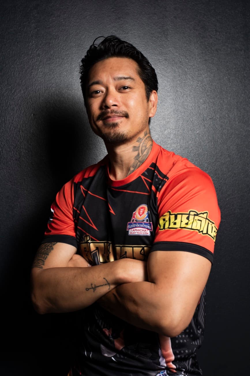 Carlo, Gründer und Lead Coach von Retro Muay Thai, mit verschränkten Armen im Trikot vor dunklem Hintergrund